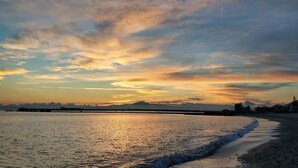 Ein Sonnenuntergang über einem ruhigen Meer mit einer fernen Küstenlinie und einer Brücke.