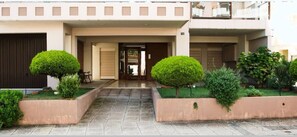 A modern building with a central entrance, two symmetrical gardens with trimmed bushes, and a tiled pathway leading to the entrance. - Amalia s Serendipity City Lights Mountain Vistas (Kalamata)
