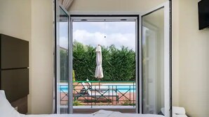 Een hotelkamer met een bed, een televisie en een balkon met uitzicht op een zwembad.