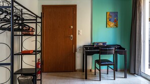 Ein Raum mit Holztür, Schreibtisch mit zwei Stühlen, einem Metallregal und einem kleinen weißen Schrank.