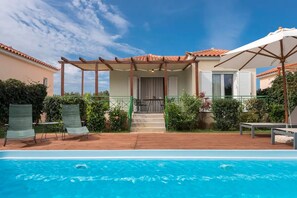 Un espace aménagé au bord de la piscine, doté d’une pergola, de sièges d’extérieur et offrant une vue sur un bâtiment dont le toit est recouvert de tuiles.