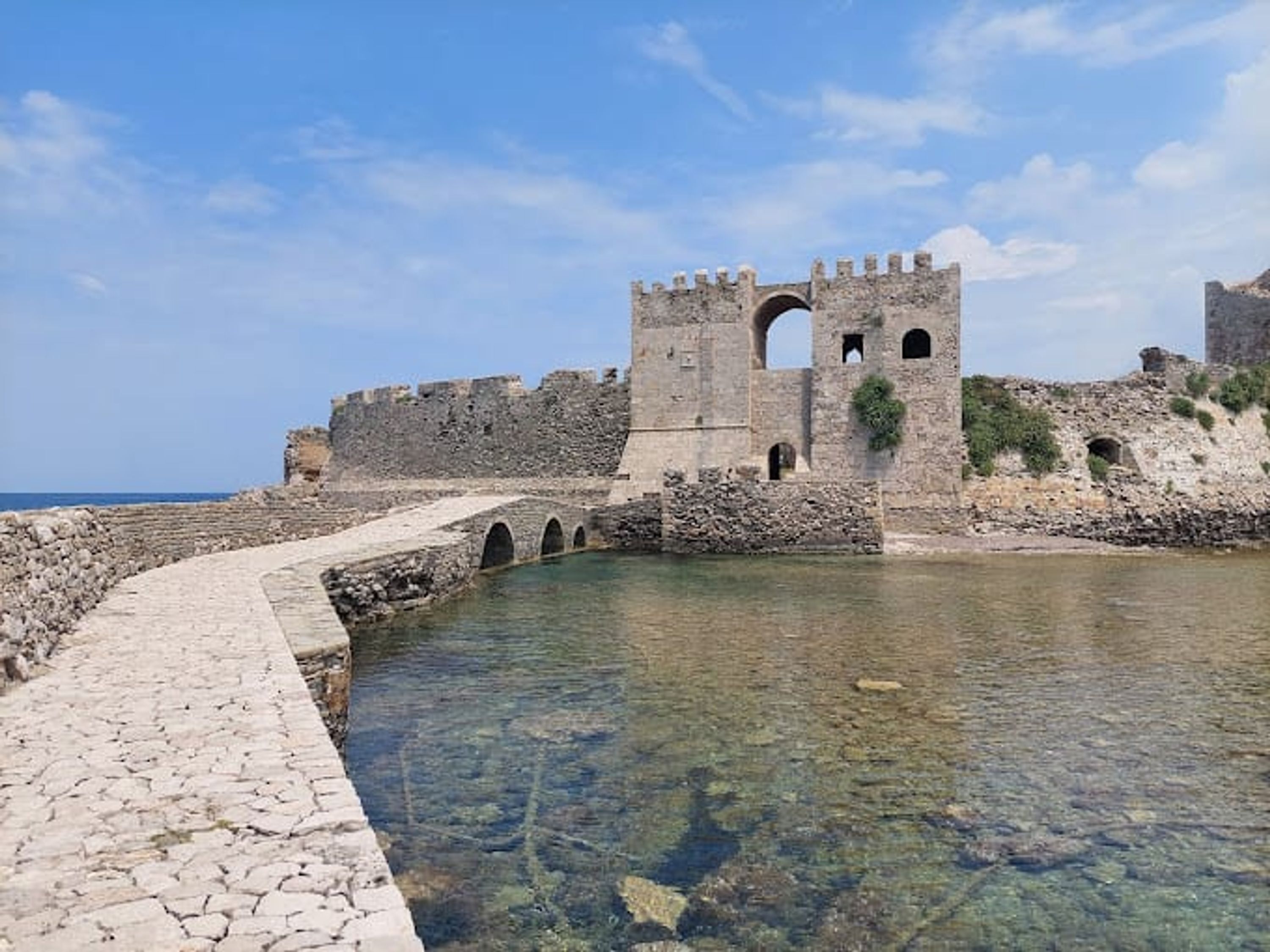 A stone pathway leading to a clear pool with a castle-like structure in the background.
