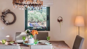 Ein Essbereich mit einem Holztisch, Stühlen, einer Blumenvase und Blick ins Freie durch ein Fenster.