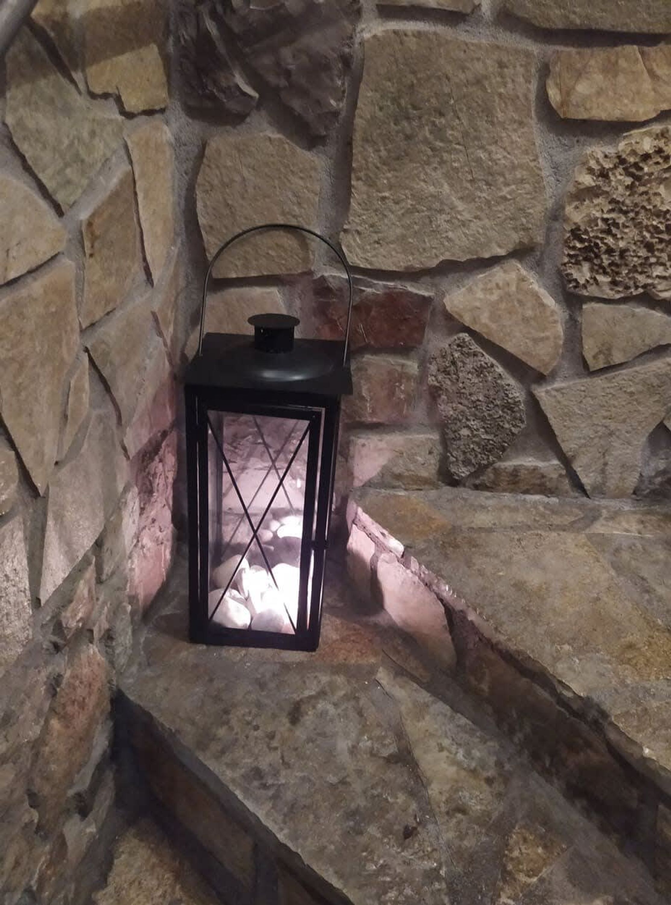 A stone wall with a black lantern on a ledge.