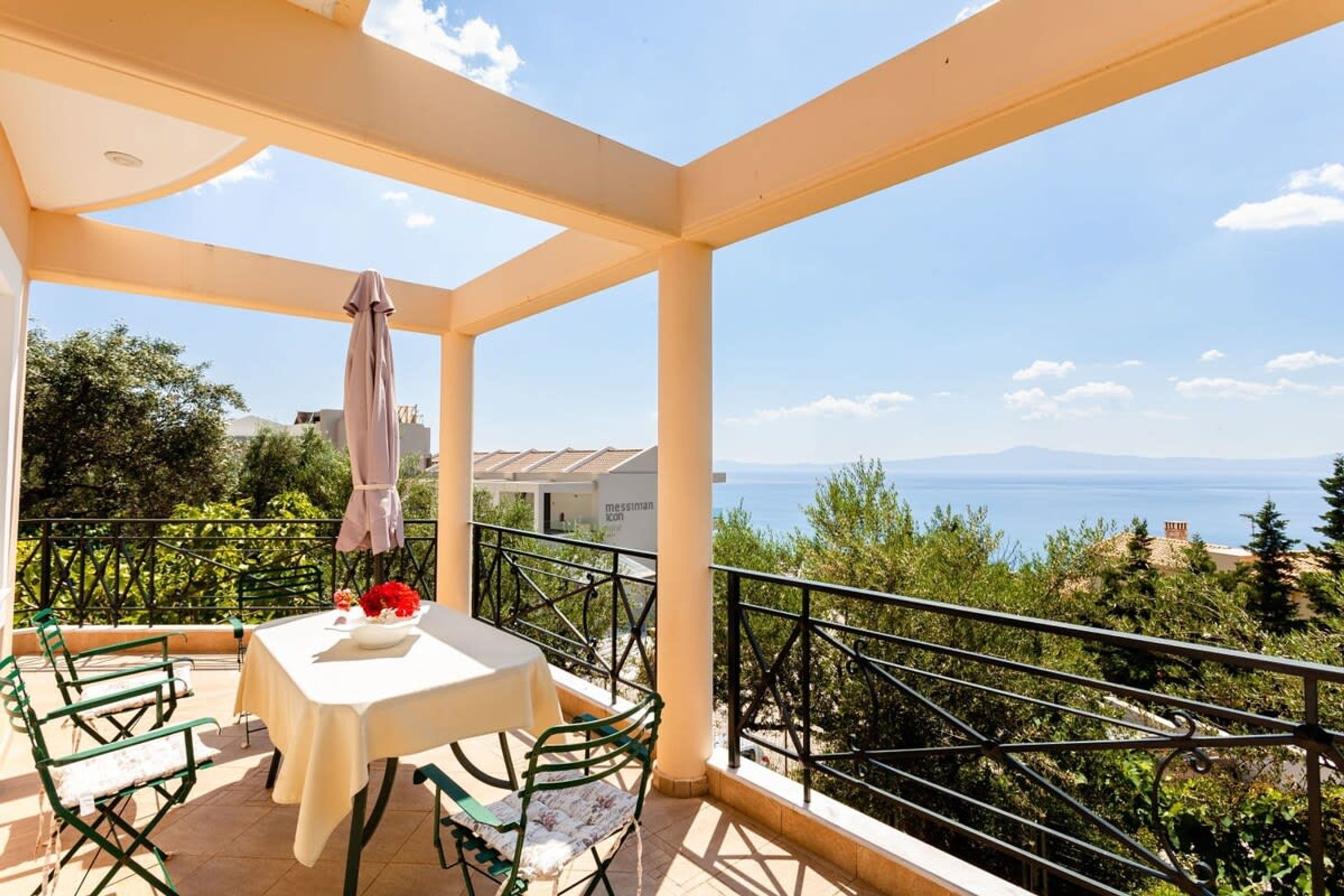 Un balcon avec une table et des chaises, une vue sur la mer et un bâtiment en arrière-plan.