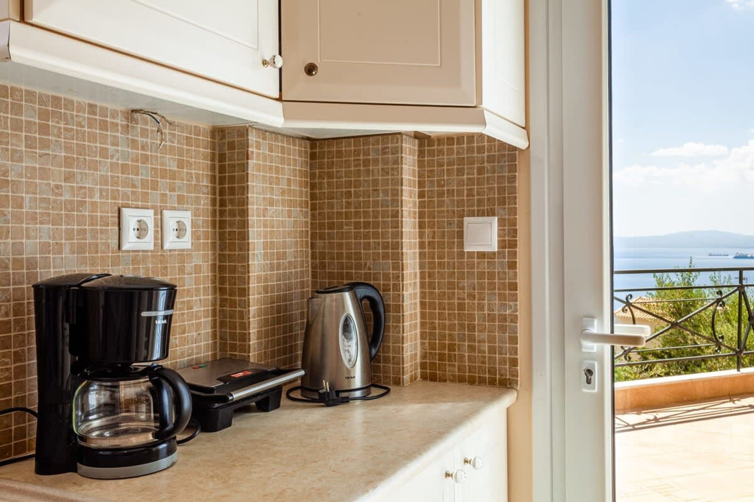 A kitchen with a coffee maker, kettle, and toaster on a tiled counter.