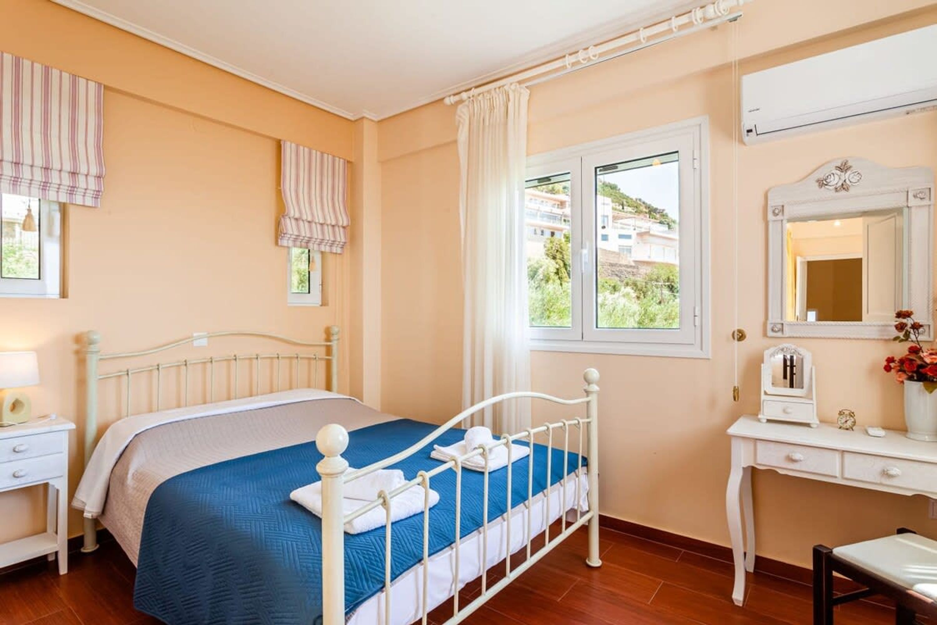 A bedroom with a bed, a bedside table, a dresser, a mirror, and a window with a view of buildings.