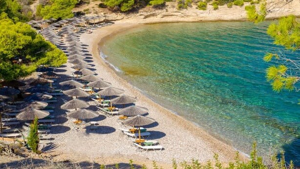 A beach with rows of sun umbrellas and lounge chairs along the shoreline. - Thalassa Return To Timeless Spetses (Spetses)