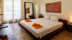 A hotel room with a large bed, a desk, a chair, a mirror, and a painting on the wall.