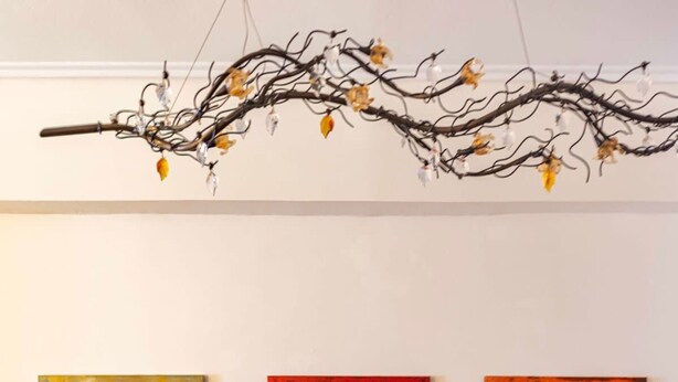 A dining area with a dark wooden table, three abstract paintings on the wall, and a branch with lights above. - Dancing on Sunshine - Melina s City Getaway (Kalamata)