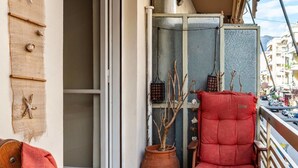 A balcony with a wooden chair and a cushioned seat, a small table with dishes, and a potted plant.