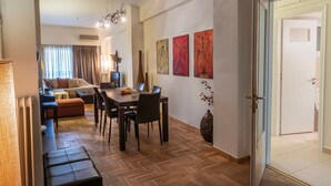 A modern living room with a dining area, featuring a wooden floor, a sofa set, a dining table with chairs, and a chandelier.