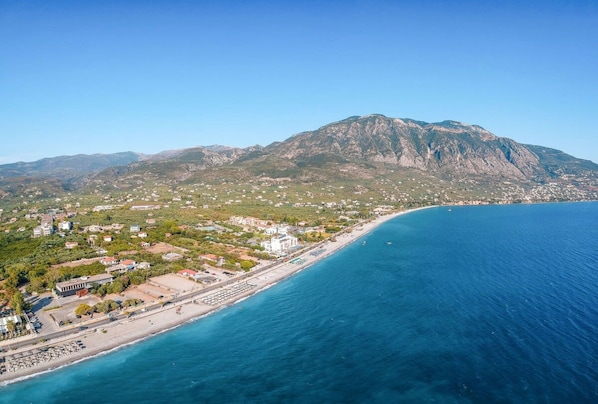 An aerial view of a coastal town with a beach, buildings, and a mountain in the background. - Nina s Villa Cosy Seaview Retreat (Kalamata)