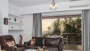 A modern living room with a leather sofa, a dining table set with glasses and plates, and a balcony with a railing. - Nina s Villa Cosy Seaview Retreat (Kalamata)