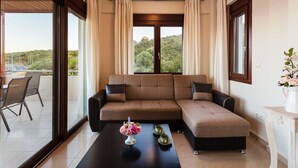A modern living room with a sectional sofa, a coffee table with a floral centerpiece, and a view of a lush green landscape through large windows.