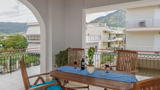 A balcony with a wooden table and chairs, a potted plant, and a bottle of wine. - Thano s Stylish Flat Just 150m to the Beach (Kalamata)