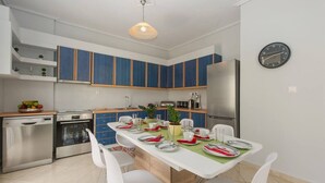 A modern kitchen with blue cabinets, a stainless steel refrigerator, and a dining area with white chairs and a green tablecloth. - Thano s Stylish Flat Just 150m to the Beach (Kalamata)