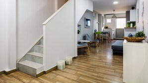 A modern interior with a staircase, wooden flooring, a dining area with chairs and a table, and a kitchen area with cabinets and a window. - Citysea Fusion Elegant Gem Minutes From the Beach (Kalamata)