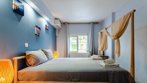 A bedroom with a bed, bedside lamps, a bedside table, a window with curtains, and a wall-mounted air conditioner. - Citysea Fusion Elegant Gem Minutes From the Beach (Kalamata)