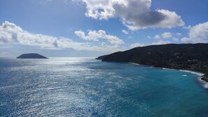 A coastal landscape with a clear sky, calm sea, and a hilly terrain.
