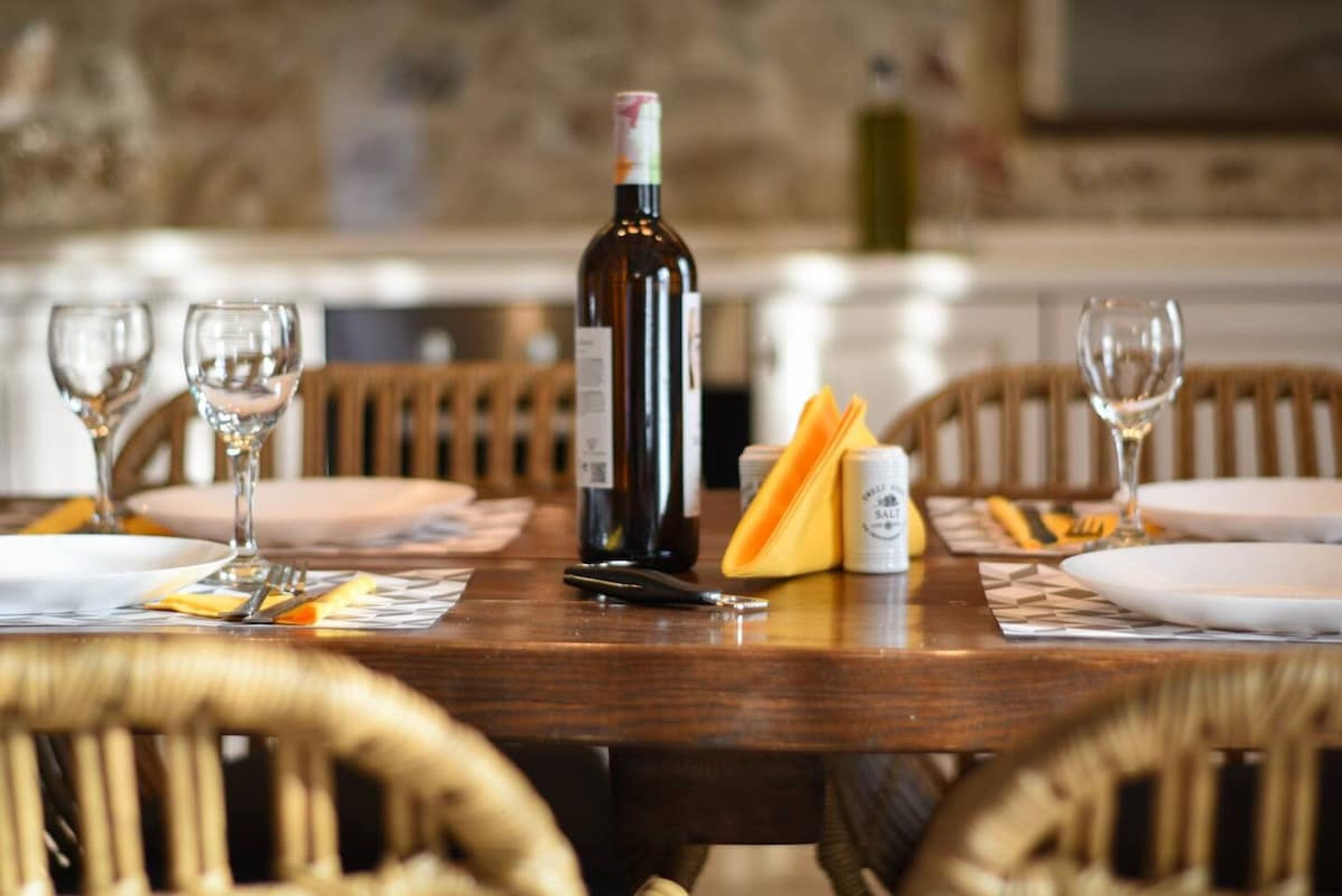 Una mesa de comedor dispuesta con copas de vino, platos, cubiertos y una botella de vino.