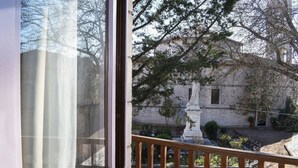 Vista desde una ventana sobre un patio con una estatua, un edificio de piedra y árboles.