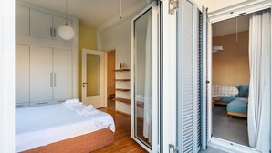 Een slaapkamer met een bed, houten vloeren, een kledingkast en een schuifdeur van glas die naar een andere kamer leidt.
