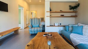 Een moderne woonkamer met een houten salontafel, een gestreept fauteuil, een bank met blauwe kussens en ingebouwde planken met decoratieve objecten.