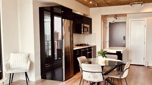 A modern kitchen with a stainless steel refrigerator, black cabinets, and a dining area with a glass table and chairs.