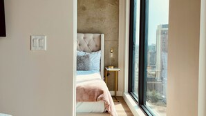 A modern bedroom with a large window, a bed with a tufted headboard, and a bedside table with a lamp.