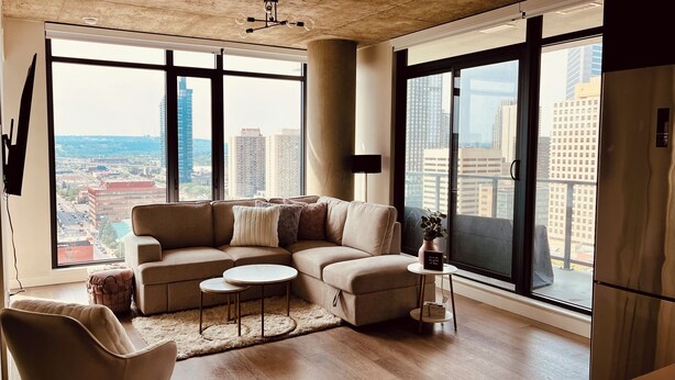 A modern living room with a sectional sofa, a round coffee table, and a view of a cityscape through large windows.