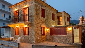 A stone building with a balcony, multiple windows, and a garage door. - Waveside Sanctuary - Luxurious Seastone Villa (West Mani)