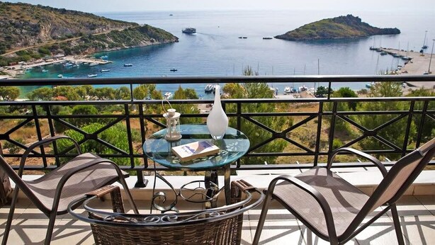 A balcony with a glass table, wicker chair, and a view of a coastal area with boats and a small island. - Coastal Paradise Found - Komis Private Pool Gem (Zakynthos)