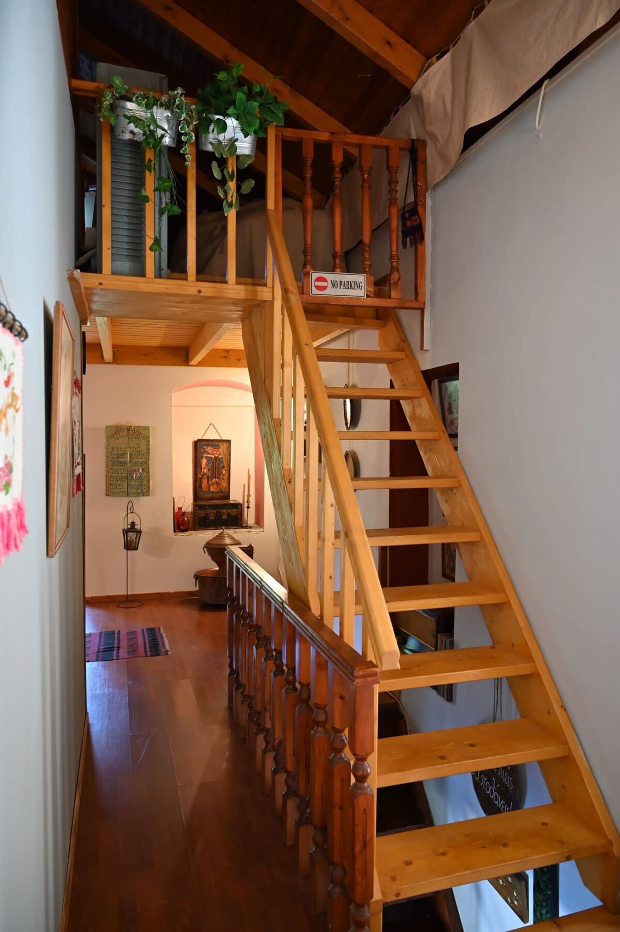 Un escalier en bois, agrémenté d’un panneau indiquant « INTERDICTION DE STATIONNER », mène à un étage supérieur doté d’un balcon orné de plantes.