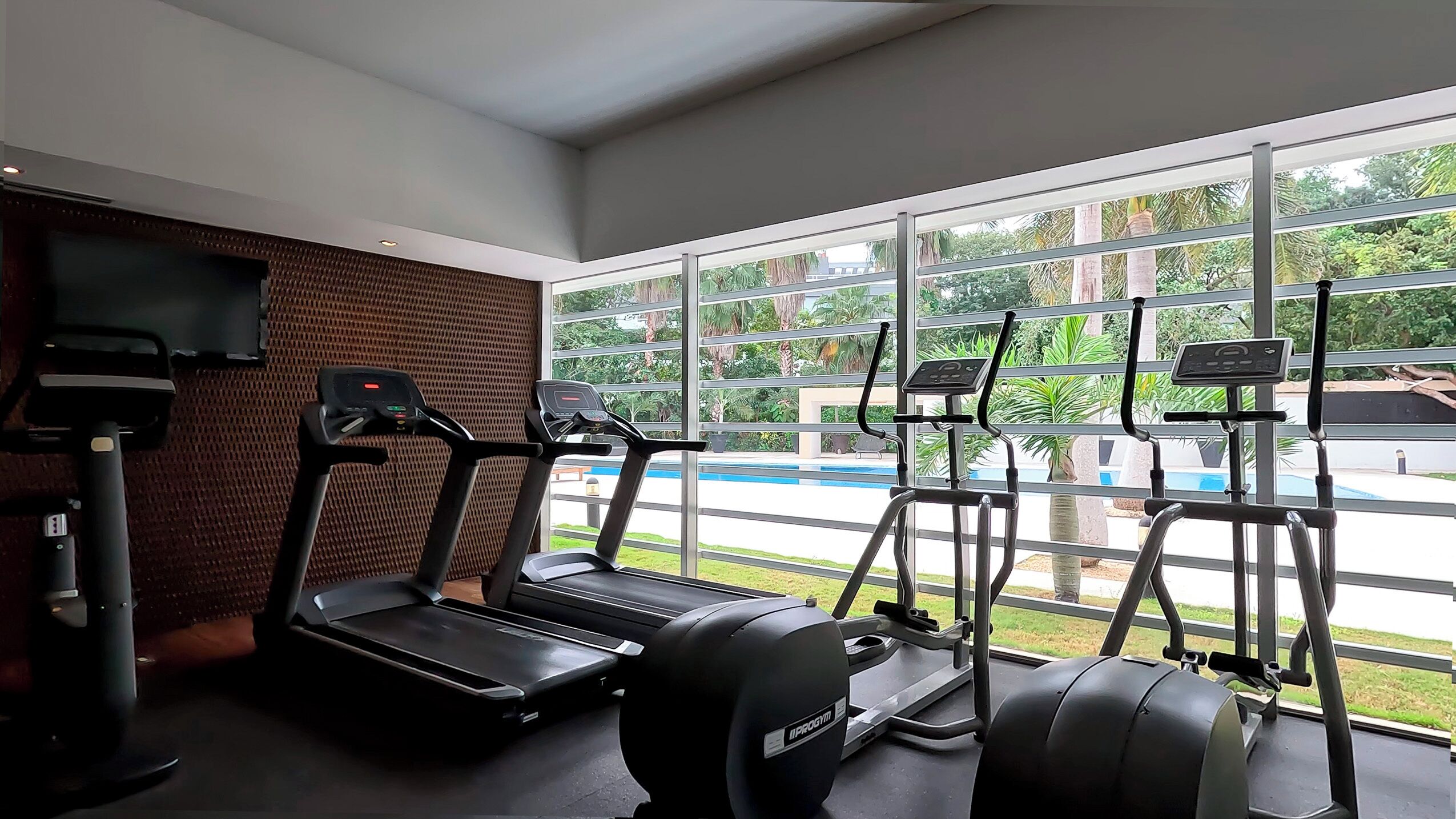 Een sportschool met loopbanden, elliptische trainers en een televisiescherm.