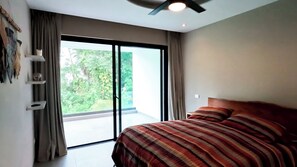 A bedroom with a large bed, a ceiling fan, and a sliding glass door leading to a balcony.