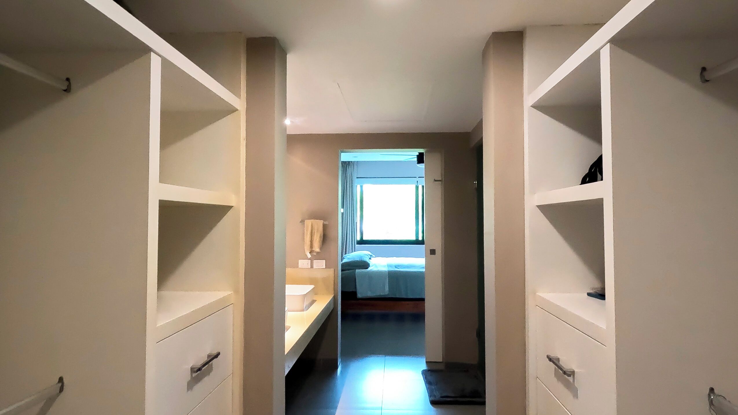 A narrow hallway with white walls and a bed at the end.
