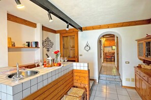 A kitchen with a wooden bench, a sink, and a dining area visible through an archway.