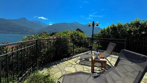 Una terraza con vistas a montañas y un lago, amueblada con sillas y una mesa.