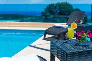 Un espace aménagé au bord de la piscine, avec des chaises longues, une table agrémentée de boissons et de fleurs, et une vue dégagée sur la piscine et la végétation environnante.