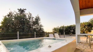 Une piscine à bordures courbes, entourée d’une terrasse en pierre et d’une pergola en bois.