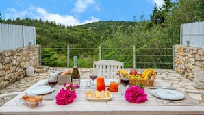 Une table de jardin, dressée à l’extérieur avec de la nourriture et des boissons, entourée de murs en pierre et offrant une vue panoramique sur les collines.