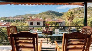 A terrace with wooden chairs and a table, overlooking a hillside with buildings and greenery. - Mani Garden Haven - Private Retreat in Stoupa (West Mani)