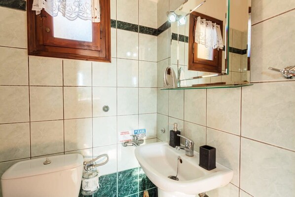 A bathroom with a toilet, sink, and mirror. There is a sign on the wall and a towel hanging on the mirror. - Mani Garden Haven - Private Retreat in Stoupa (West Mani)