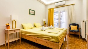 A hotel room with a wooden bed, a desk with a lamp, a chair, and a window with curtains. - Zografou s Hidden Gem - Athens Charming Home (Zografos)