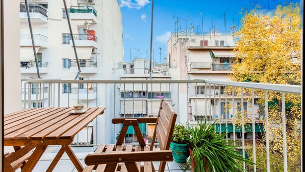 A balcony with a wooden table and chairs, potted plants, and a view of surrounding buildings. - Zografou s Hidden Gem - Athens Charming Home (Zografos)