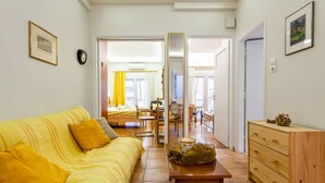 A bright living room with a yellow sofa, a wooden table, and a mirror. There is a kitchen area in the background with a dining table and chairs. - Zografou s Hidden Gem - Athens Charming Home (Zografos)