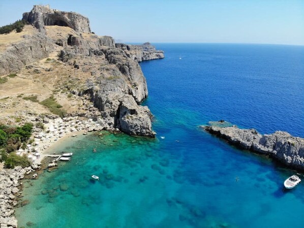 A coastal landscape with rocky cliffs, clear turquoise waters, and a small beach area with boats.
