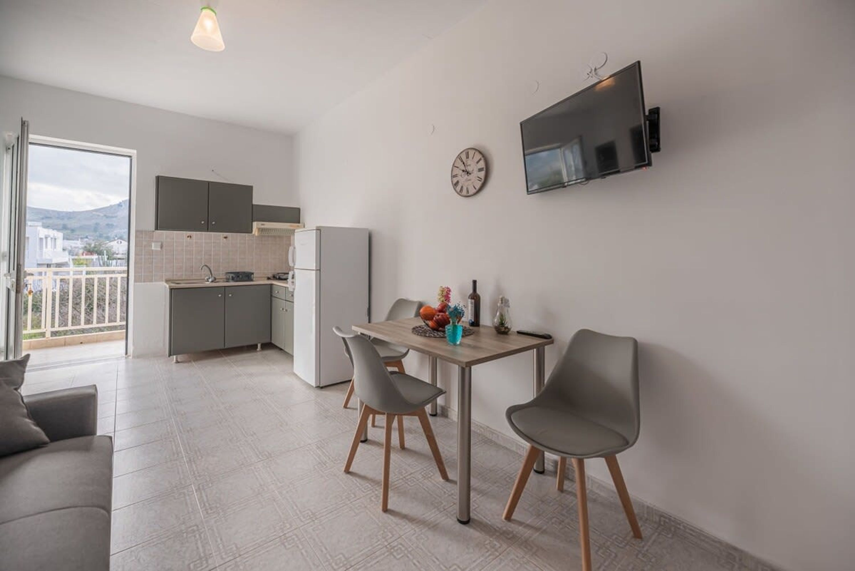 A modern kitchen with grey cabinets, a dining area with a table and chairs, and a TV mounted on the wall.