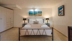 A bedroom with a bed, two bedside tables, a wardrobe, and artwork on the walls. - Mani s Aura Seaside-enchanting Stone Gem (West Mani)